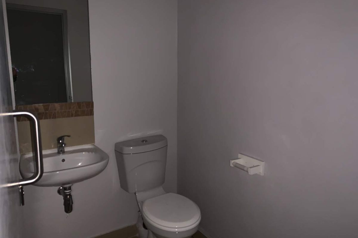 A functional, minimalist bathroom featuring a wall-mounted basin, standard toilet, and safety grab rail, providing essential facilities in a clean, neutral space.