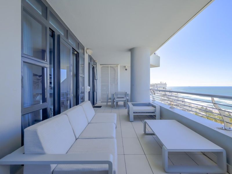 A spacious, modern balcony featuring tiled flooring, a sleek glass balustrade, and expansive ocean views, accessible via large sliding glass doors.