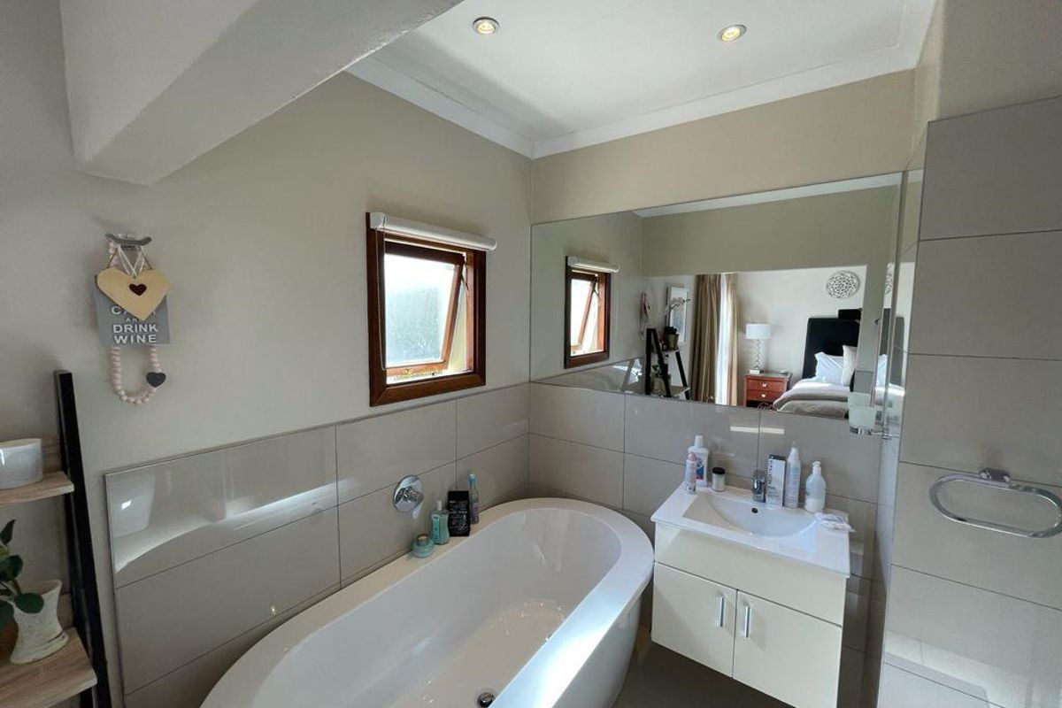 Modern bathroom featuring a sleek freestanding bathtub, wall-mounted vanity with integrated basin, and a large mirror, finished with neutral wall tiles and recessed lighting.