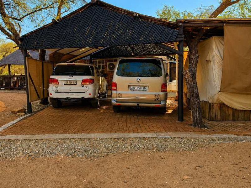A covered outdoor parking area featuring a thatched roof structure supported by timber posts with a paved surface.