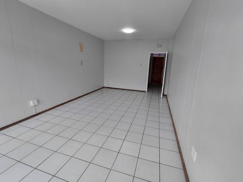 An empty, neutrally painted living area featuring tiled flooring and a simple ceiling light fixture, providing a blank canvas for interior design.