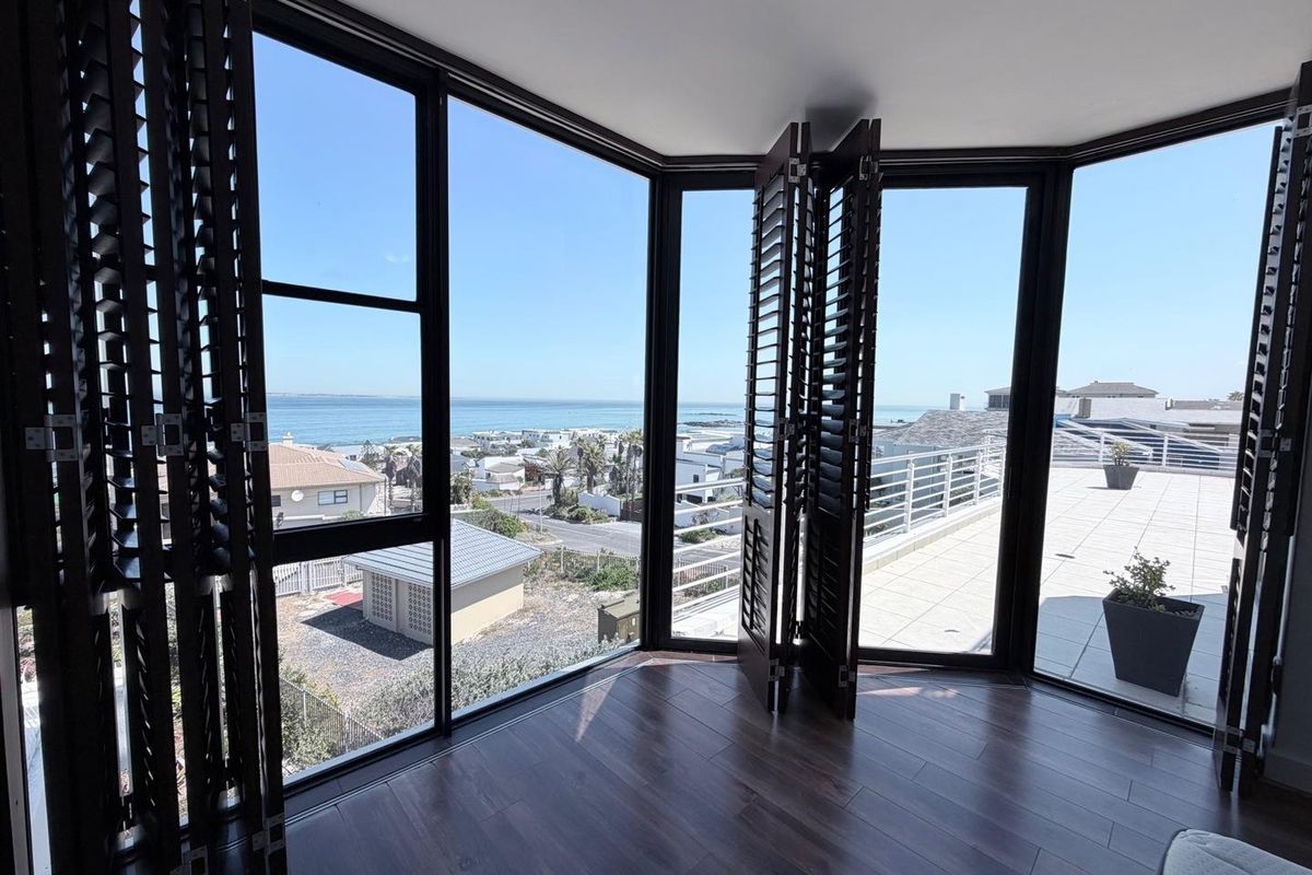 Bright living area featuring expansive floor-to-ceiling windows with folding shutters, offering panoramic coastal views and direct access to a spacious outdoor terrace.