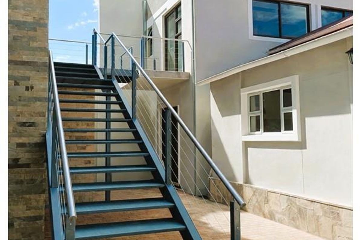 Exterior view of the property rear featuring a modern metal staircase with cable railing leading to an upper level balcony.