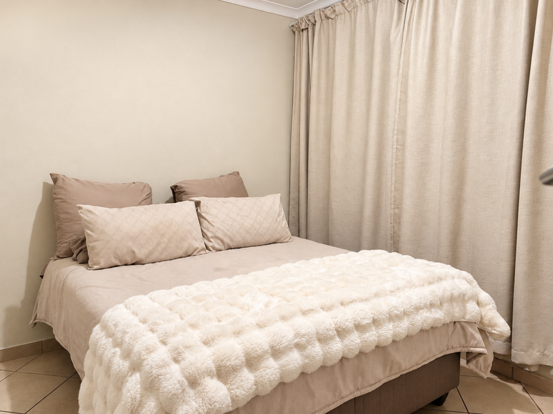A cozy bedroom featuring neutral wall tones, tiled flooring, and floor-to-ceiling curtains.