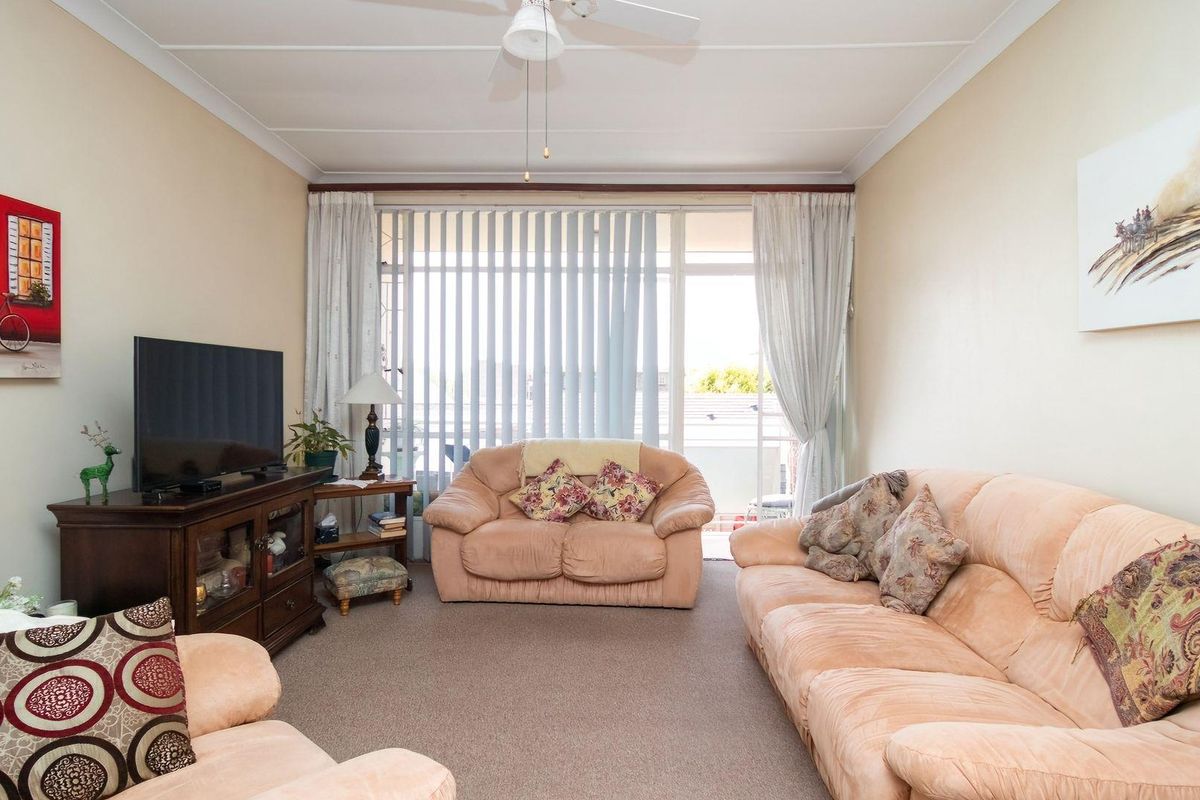 A comfortable living room featuring neutral carpeting, a ceiling fan, and large sliding glass doors that provide access to an outdoor balcony area.