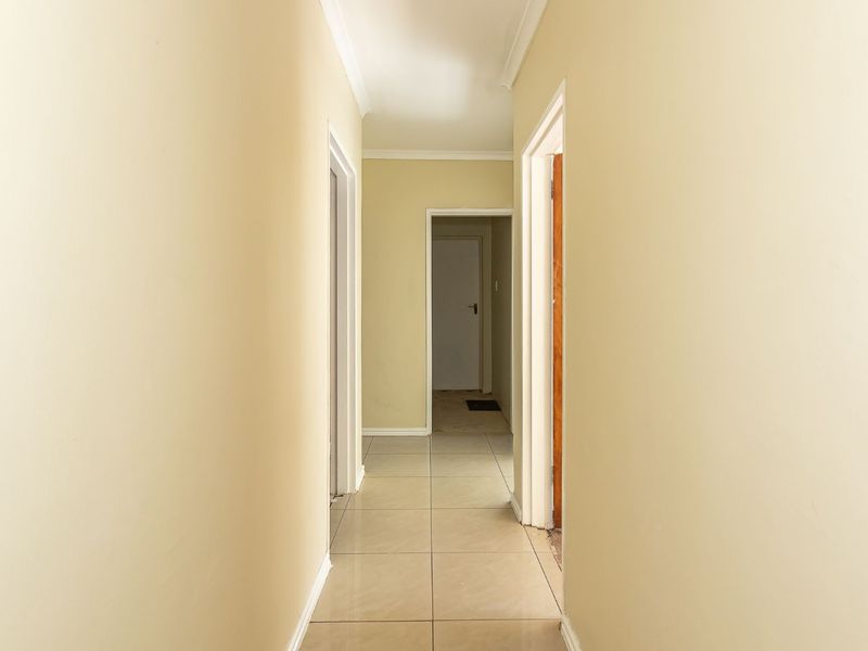 A clean, neutral-toned hallway featuring tiled flooring, coving, and multiple internal doorways providing access to various rooms.