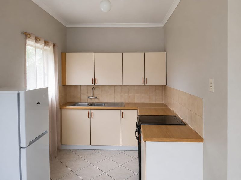 A functional kitchen featuring light-toned cabinetry, laminate countertops, a tiled backsplash, and a built-in electric hob with a stainless steel sink.
