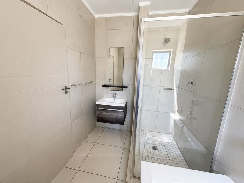 A modern, clean bathroom featuring a floating vanity, a glass-enclosed shower, and neutral floor-to-ceiling tiling.