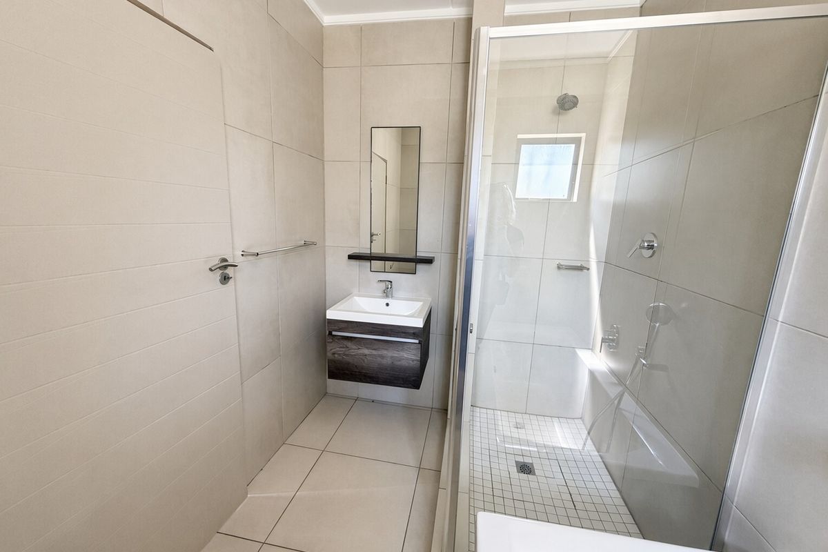A modern, clean bathroom featuring a floating vanity, a glass-enclosed shower, and neutral floor-to-ceiling tiling.