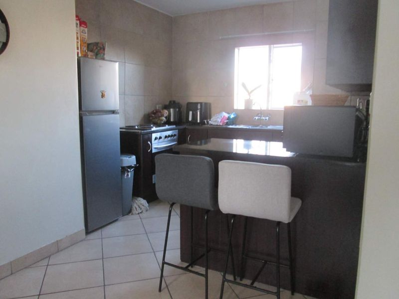 A functional kitchen featuring dark cabinetry, granite countertops, a stainless steel stove, and tiled flooring with a breakfast bar area.