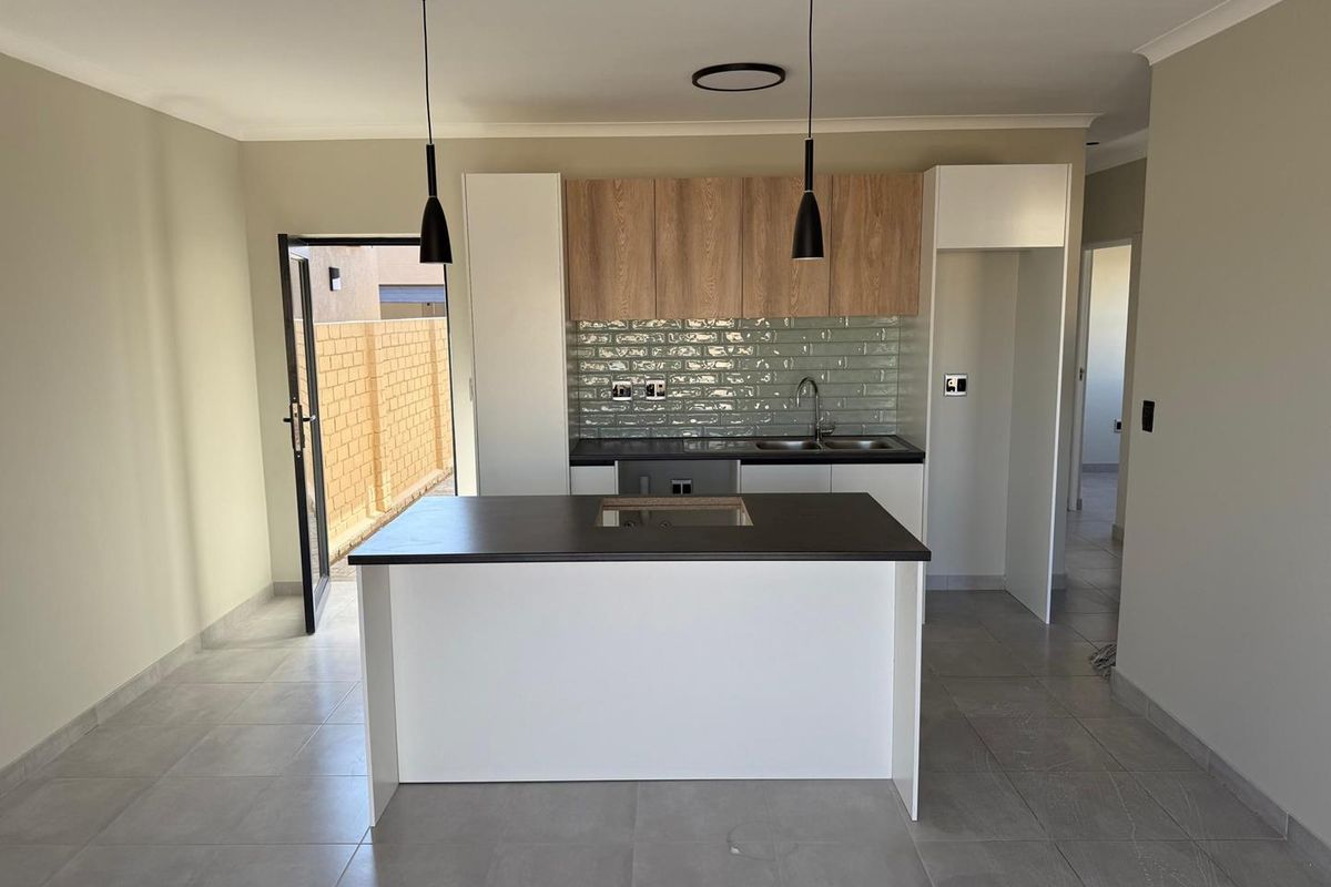 Modern open-plan kitchen featuring a central island, light wood-tone cabinetry, subway tile backsplash, and tiled flooring with direct access to the exterior.