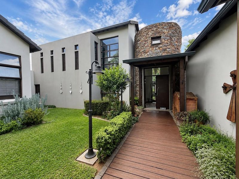 A modern architectural entrance featuring a stone-clad turret, timber walkway, and landscaped garden, creating a welcoming and sophisticated facade.