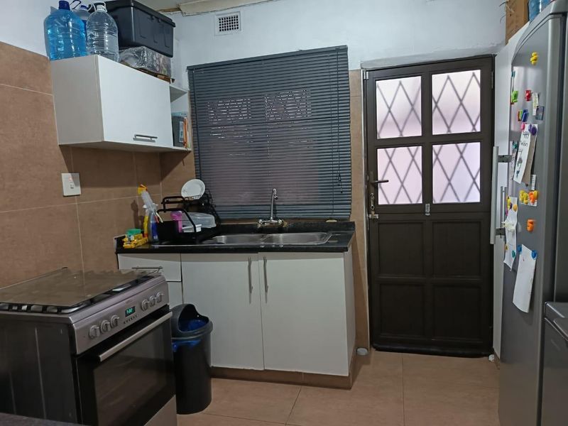 Compact kitchen featuring built-in cabinetry, granite countertops, double sink, and direct access to an exterior security door.