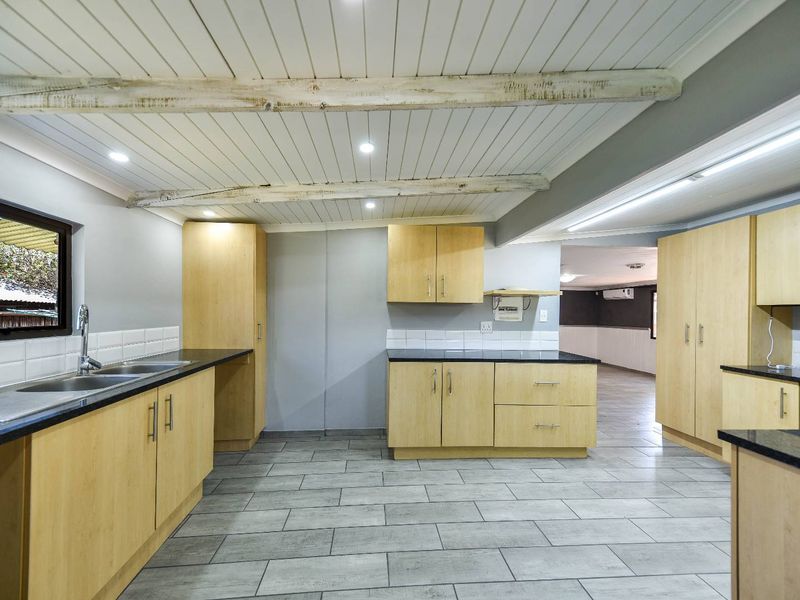 Spacious kitchen featuring light wood cabinetry, dark granite countertops, tiled flooring, and distinctive exposed timber ceiling beams.
