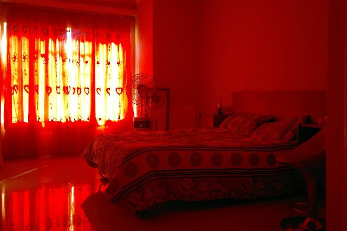 A bedroom featuring tiled flooring and a large window with curtains, currently illuminated by strong red ambient lighting.