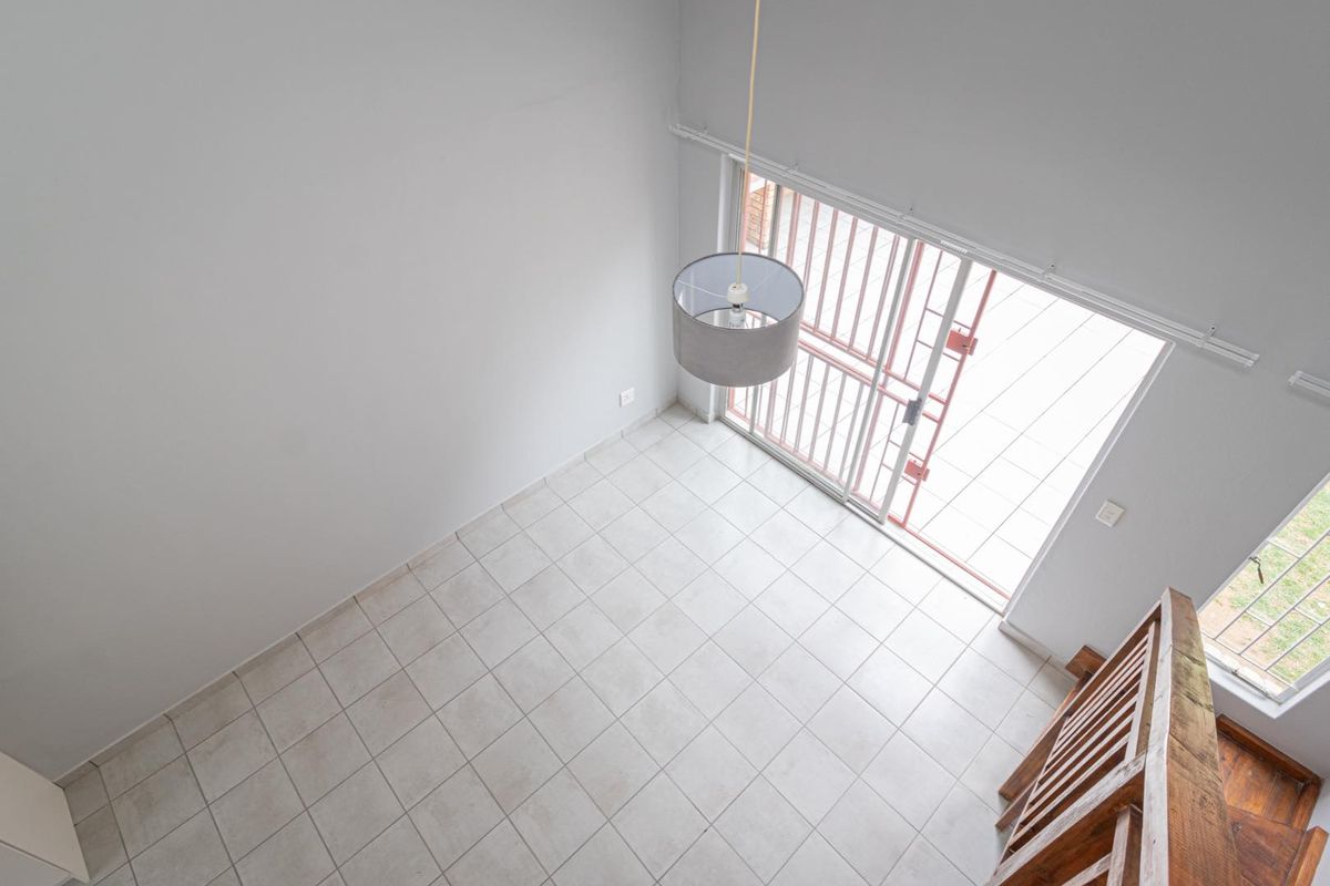 An elevated view of an empty, tiled living area featuring a sliding door with security gate and access to a wooden staircase.