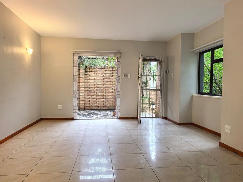 An empty, well-lit living area featuring neutral tiled flooring, a security gate, and direct access to an outdoor patio space.