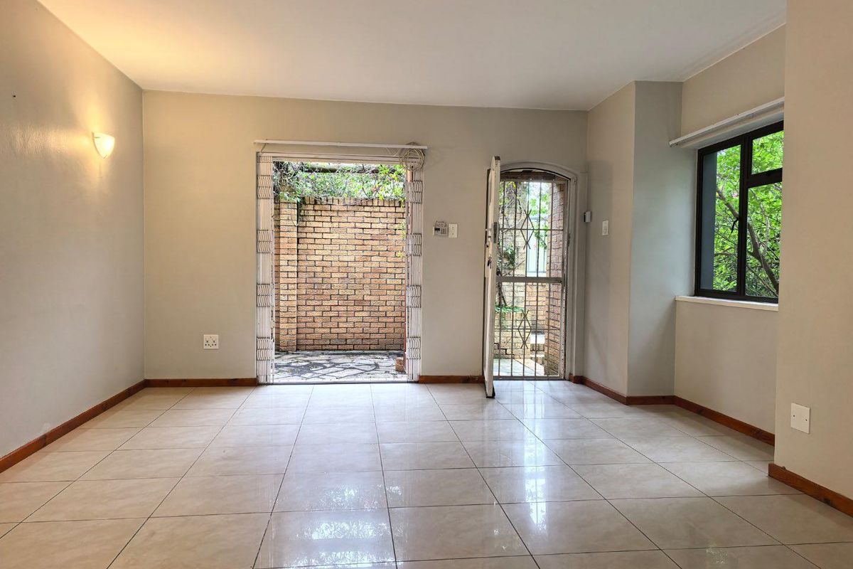 An empty, well-lit living area featuring neutral tiled flooring, a security gate, and direct access to an outdoor patio space.