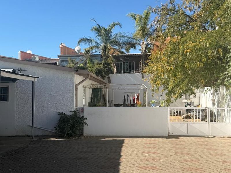 A paved rear courtyard area featuring a boundary wall, metal gate, and mature trees, providing a functional outdoor space.