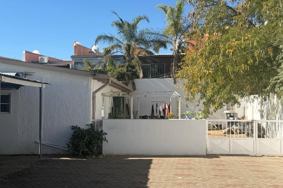 A paved rear courtyard area featuring a boundary wall, metal gate, and mature trees, providing a functional outdoor space.