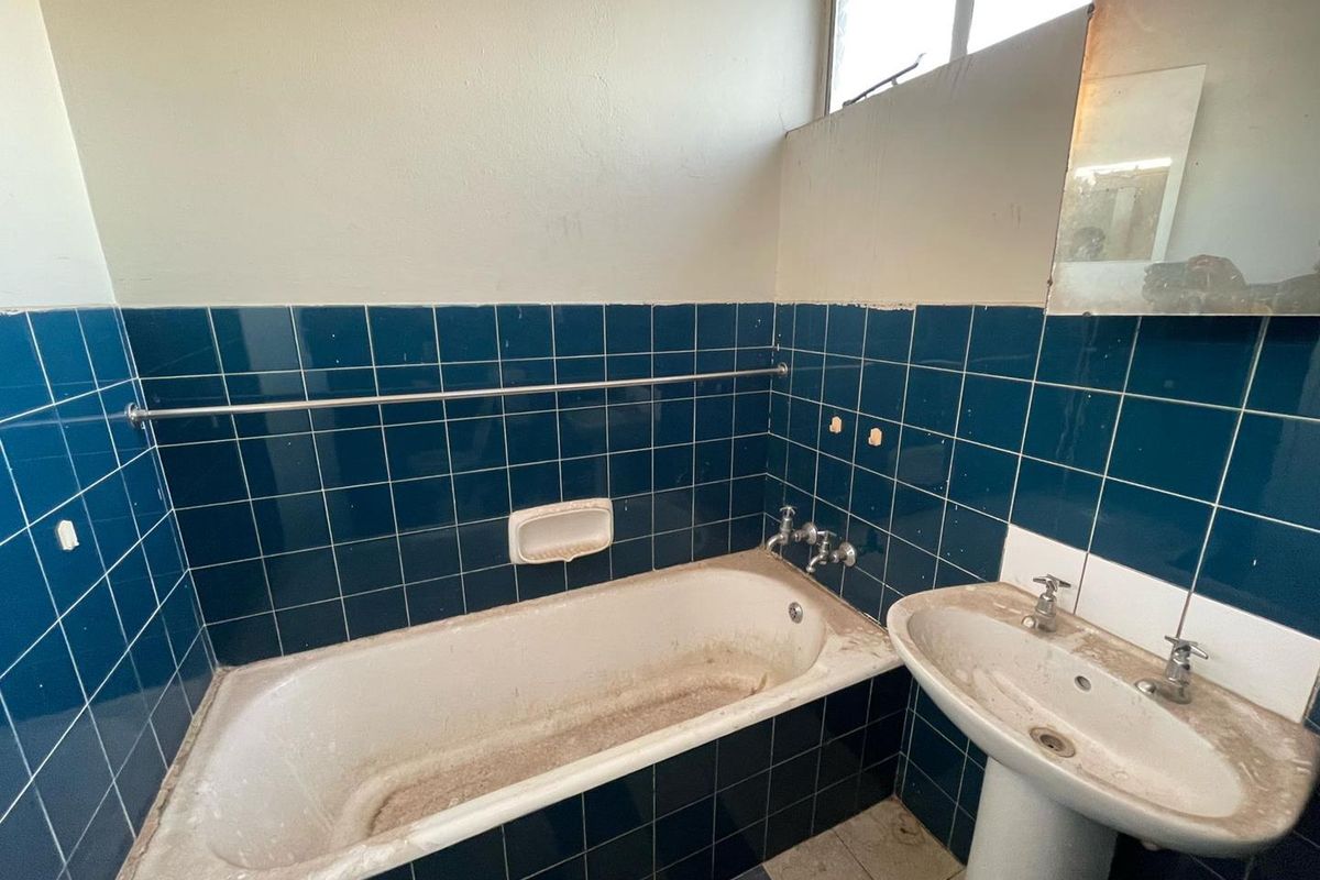 A dated bathroom featuring dark blue wall tiles, a pedestal basin, and a bathtub, requiring significant renovation and modernization of fixtures and finishes.