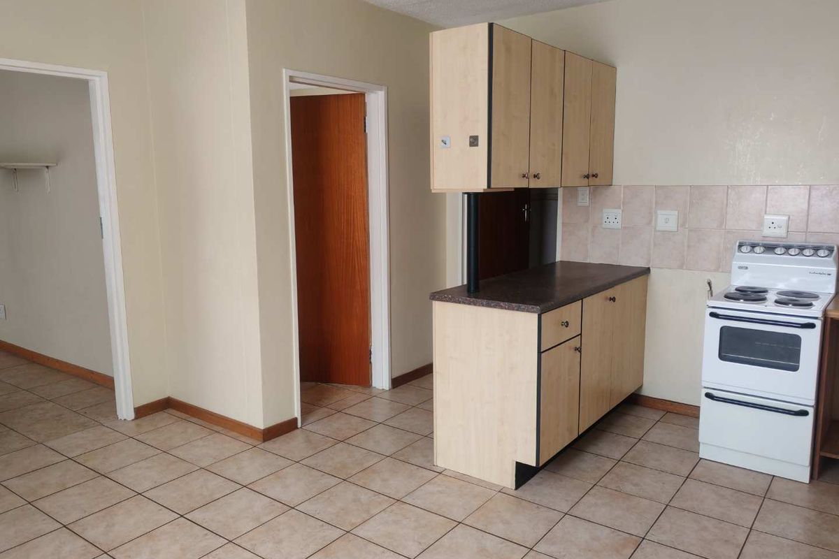 A functional kitchen area featuring laminate cabinetry, tiled flooring, and a tiled backsplash, offering a blank canvas for potential modern updates.