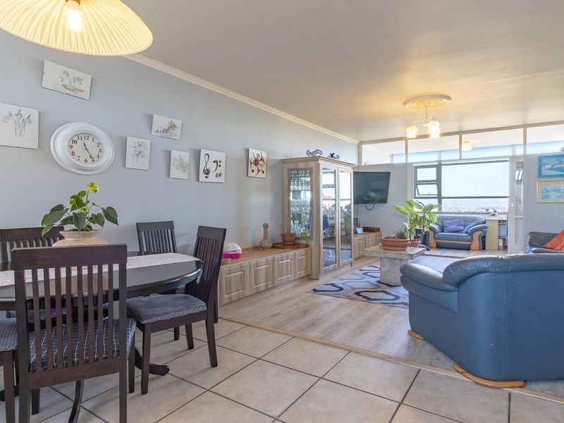 Spacious open-plan living and dining area featuring a mix of tiled and laminate flooring, large windows, and classic ceiling detailing.