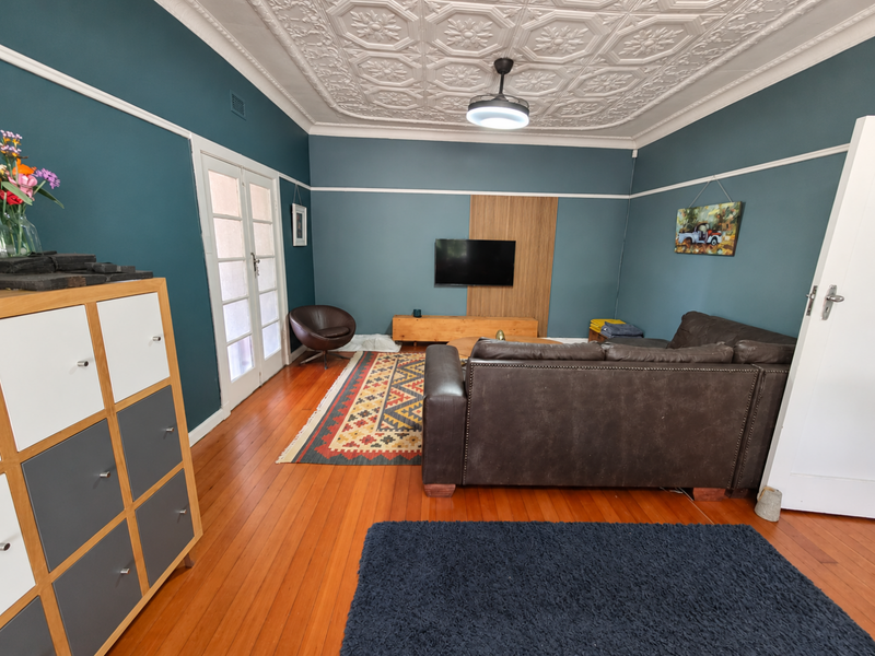A well-maintained living room featuring original hardwood flooring, a decorative pressed metal ceiling, and classic picture rails, creating a character-filled living space.
