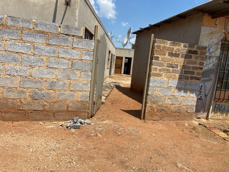 View of the property entrance featuring a concrete block boundary wall, metal gate, and access path leading to the main building structure.