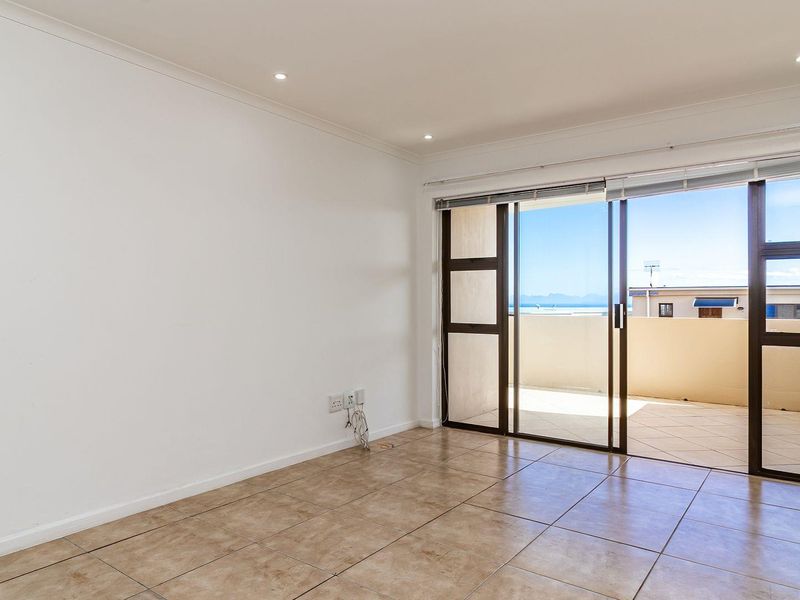 An empty, well-lit living room featuring tiled flooring, recessed lighting, and a large sliding glass door providing access to a balcony with scenic views.