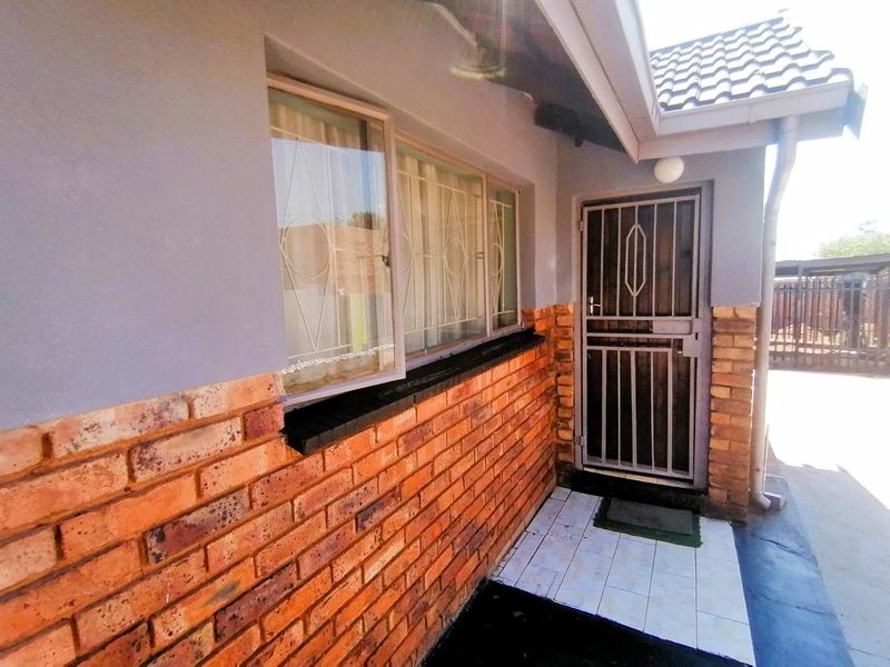 Front entrance area featuring a secure metal gate, brick facade detailing, and tiled flooring under a covered roof section.
