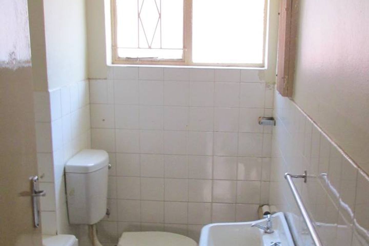 A dated bathroom featuring a wall-mounted basin, toilet, and tiled splashback, requiring renovation to update the finishes and flooring.