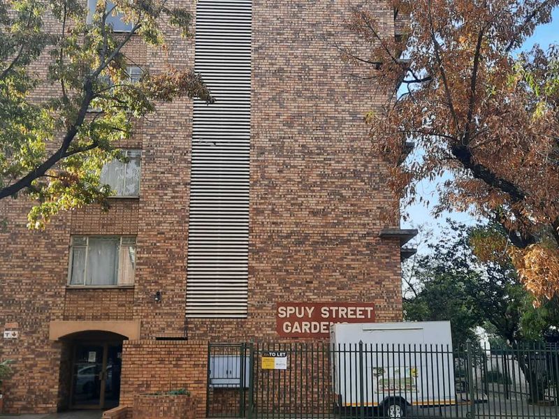 Exterior view of the Spuy Street Gardens apartment building, featuring a classic brick facade and secure perimeter fencing.