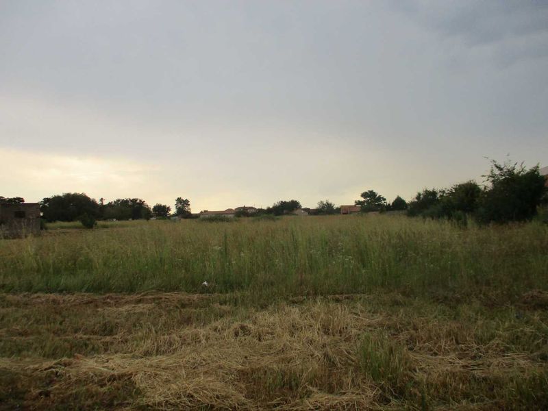A view of a vacant residential plot featuring open grassland and surrounding neighborhood vegetation.