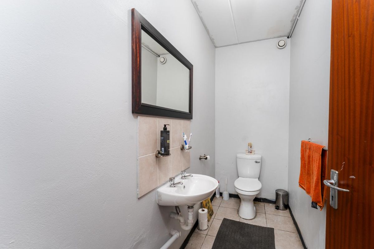 A compact office bathroom featuring a ceramic washbasin, dual-flush toilet, and tiled flooring, requiring minor cosmetic updates to the ceiling and finishes.