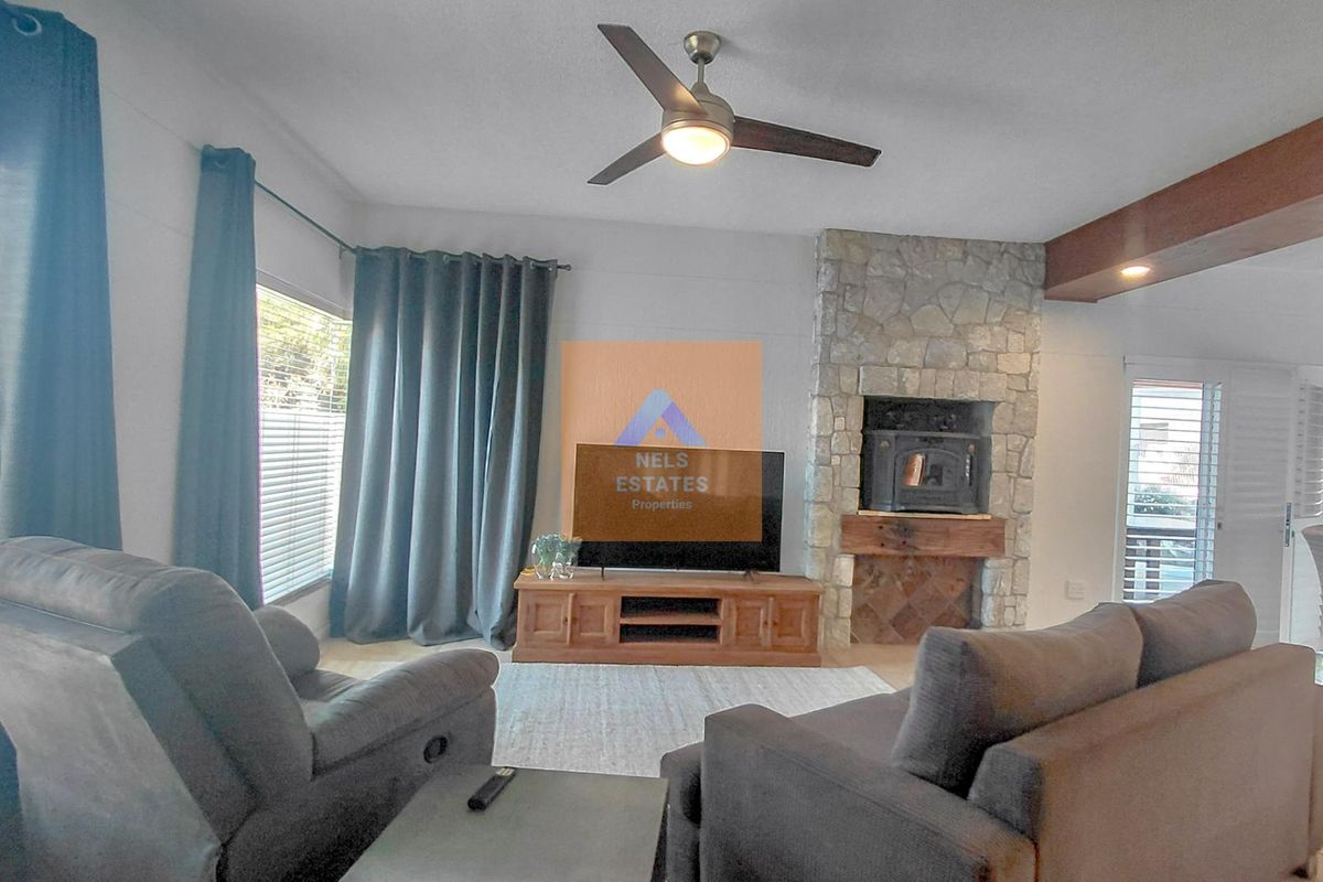 A comfortable living room featuring a prominent stone fireplace with a wood mantel, ceiling fan, and recessed lighting, creating a warm and inviting atmosphere.