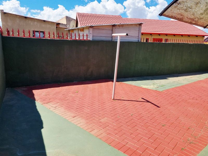 A paved rear courtyard area featuring a perimeter wall with security spikes and a fixed washing line.