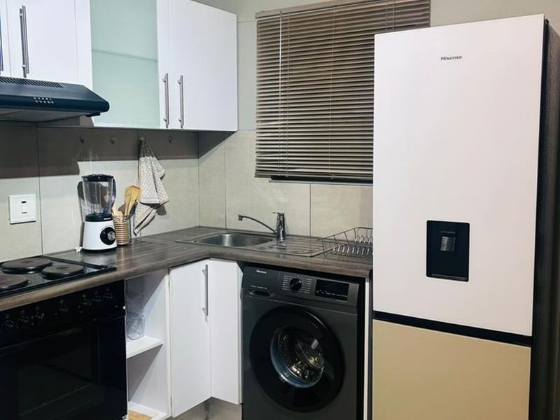 A compact, modern kitchen featuring white cabinetry, dark laminate countertops, integrated oven and hob, and tiled flooring with a neutral color palette.