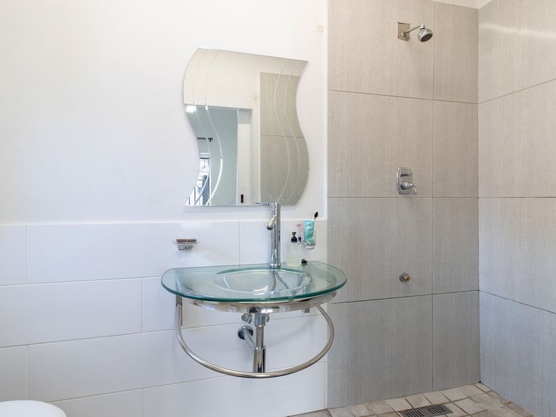 A modern bathroom featuring a wall-mounted glass basin, chrome fixtures, and a tiled shower enclosure with a linear drain.