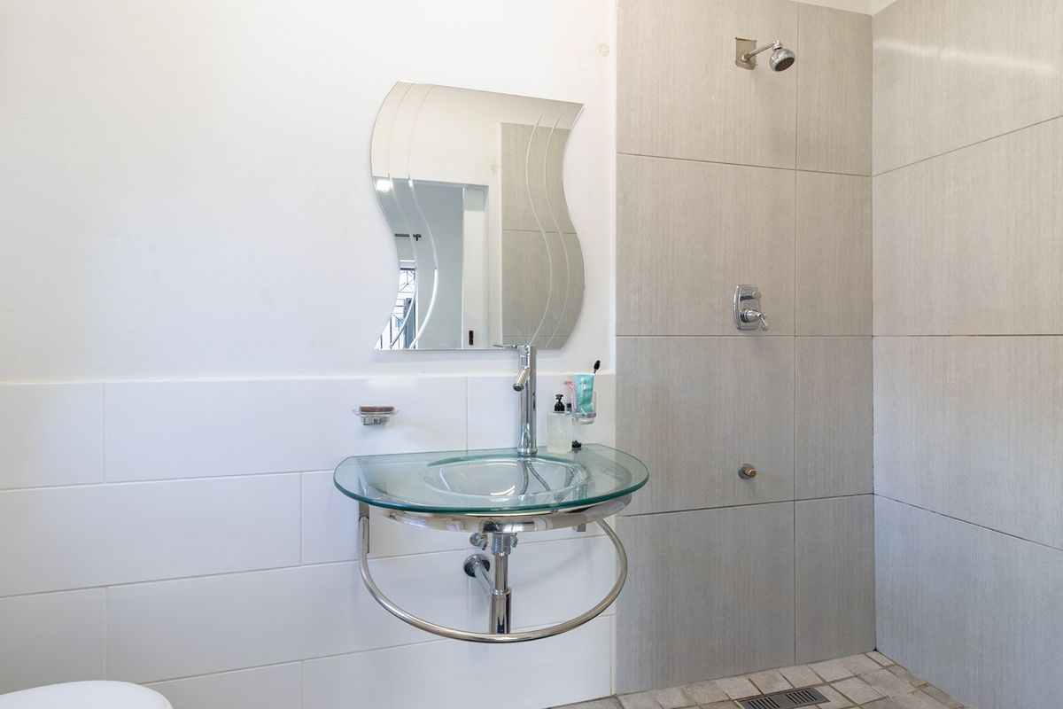 A modern bathroom featuring a wall-mounted glass basin, chrome fixtures, and a tiled shower enclosure with a linear drain.