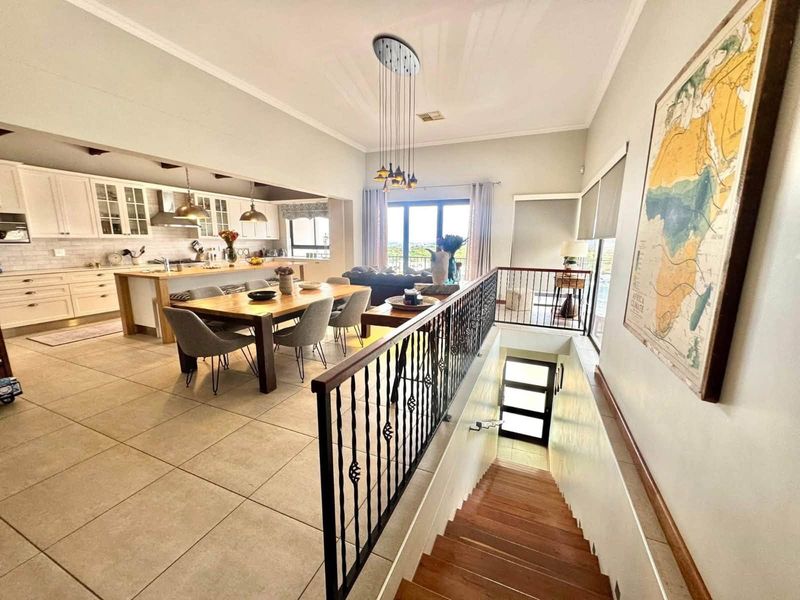 Spacious open-plan living area featuring a modern kitchen with island, dining space, and a wooden staircase with decorative wrought iron balustrade.
