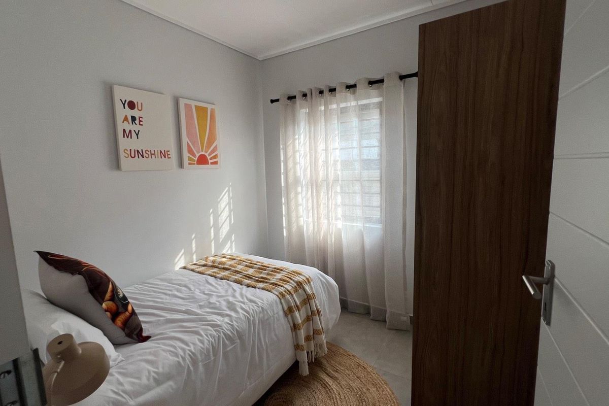 A bright and compact bedroom featuring neutral wall finishes, tiled flooring, and a built-in wooden door.