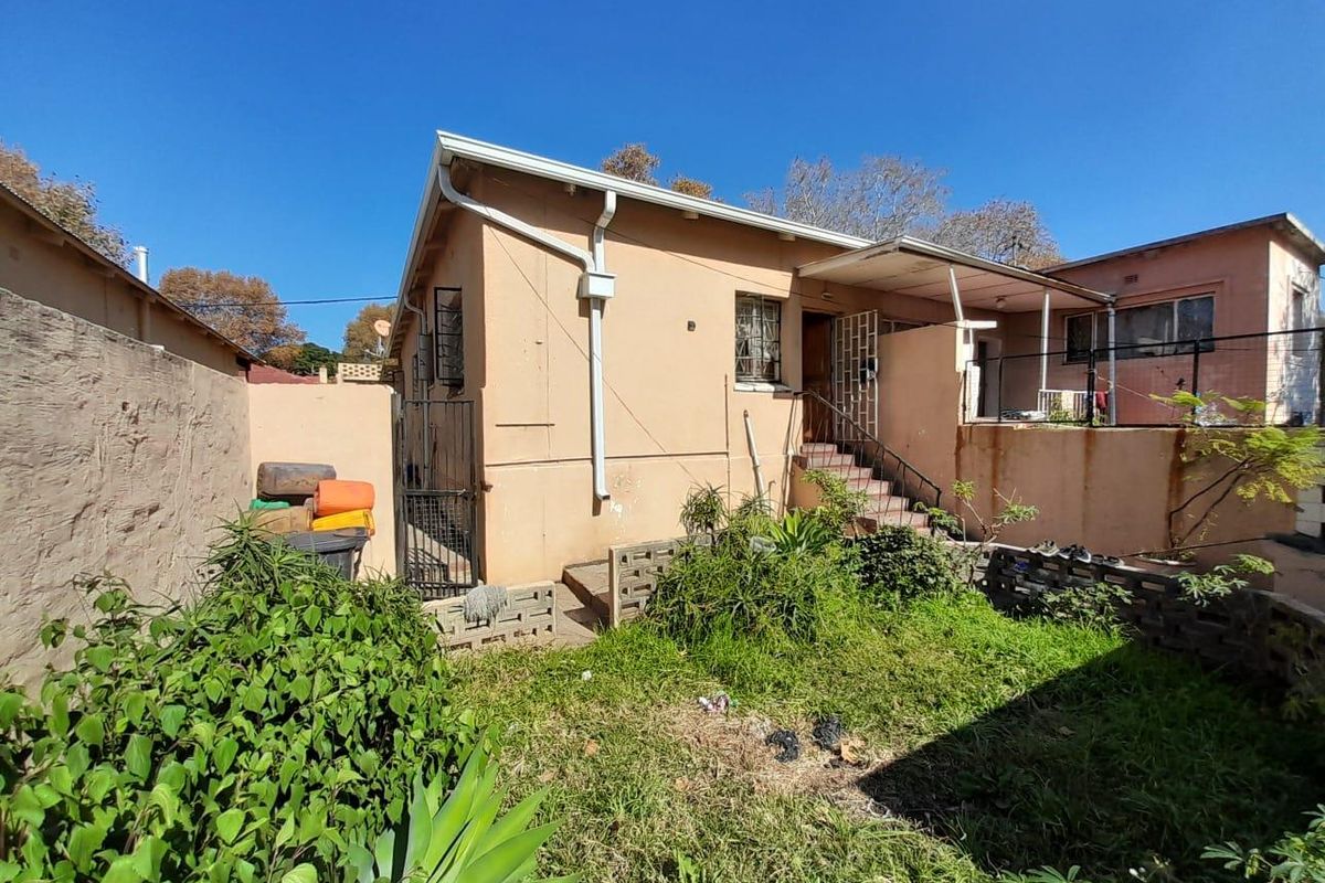 Rear view of the property showing a small garden area, concrete stairs leading to the entrance, and security features on windows and doors.