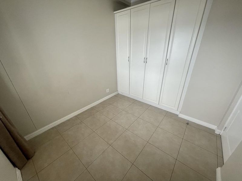 A clean, empty bedroom featuring neutral tiled flooring and a large, white built-in wardrobe with ample storage space.