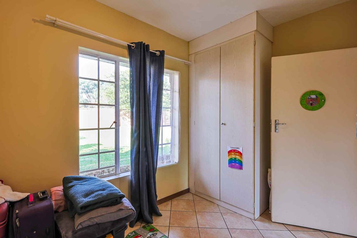 A bedroom featuring built-in cupboards, tiled flooring, and a window overlooking the garden area.
