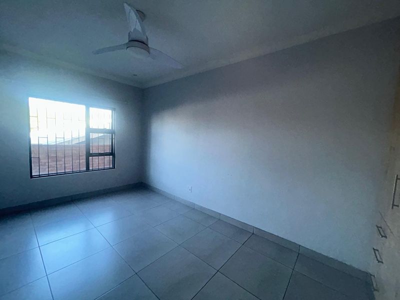 An empty bedroom featuring tiled flooring, a ceiling fan, and built-in cupboards, with security bars installed on the window.