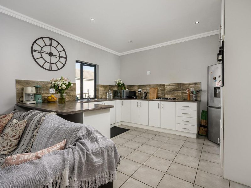 An open-plan kitchen featuring white cabinetry, laminate countertops, tiled splashbacks, and neutral floor tiles, seamlessly integrated with the adjacent living area.