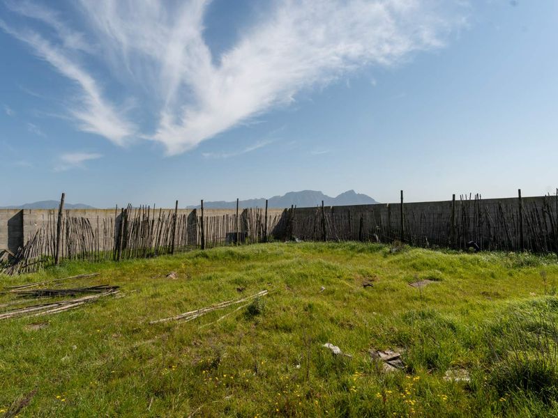 A vacant residential plot featuring a perimeter boundary wall and weathered wooden pole fencing with mountain views in the background.