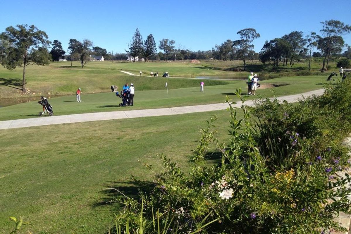 A scenic view of a well-maintained golf course featuring lush green fairways, landscaped grounds, and a water feature.
