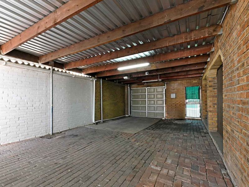 A functional, covered garage space featuring exposed timber rafters, brick walls, and durable paved flooring with a sectional garage door.